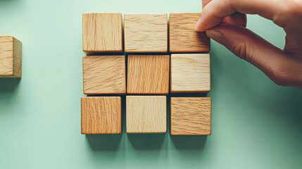 A person is putting a wooden block into a square of wooden blocks