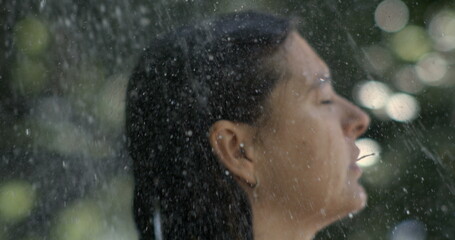 Profile of woman enjoying outdoor shower, water streaming in slow-motion at 800 fps, eyes closed,...