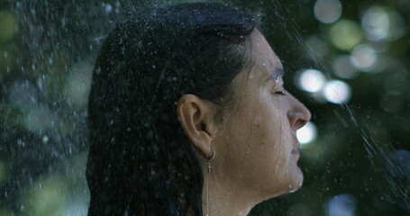 Side profile of woman under outdoor shower, water streaming down face in slow-motion at 800 fps,...