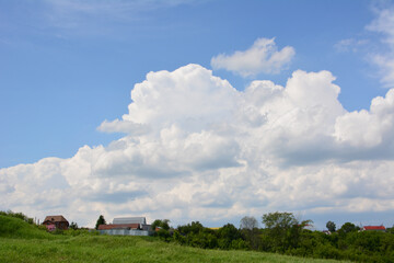 a house is in a field with a large cloud in the sky 