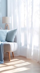 A cozy living room corner with a plush grey armchair, soft blue pillows, and a lamp, bathed in the warm glow of sunlight streaming through a sheer white curtain.
