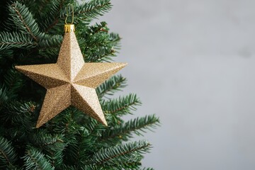 A shimmering gold star ornament hangs from a Christmas tree, surrounded by lush green branches against a soft gray background.