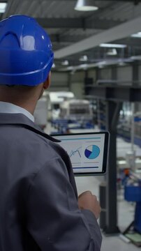 African American man with a blue helmet in a factory unit, an engineer looking at graphs on a tablet checking an automatization process, side view.