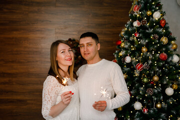 A romantic pair is hugging and holding Bengal lights in front of a Christmas tree