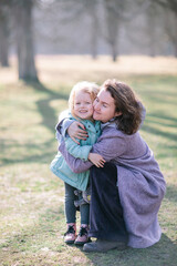 Fototapeta premium Young beautiful mother and an adorable blond little daughter are hugging and in a park in spring, happy family
