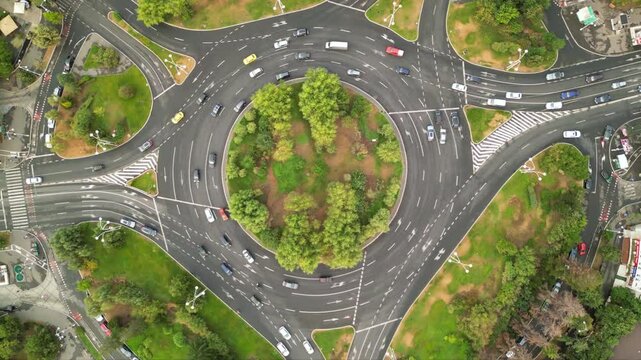 High angle drone footage of Herastrau and Piata aviatorilor Bucharest Romania. Green roundabout seen on a sunny day during golden hour. Traffic navigating a rotary intersection. Flowing traffic.
