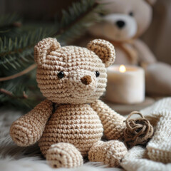 A small crocheted teddy bear with brown yarn sits on a soft blanket with a white candle and yarn ball nearby.