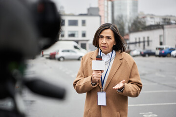 A dedicated journalist in a beige coat delivers a live report, engaging with the audience in a city setting.