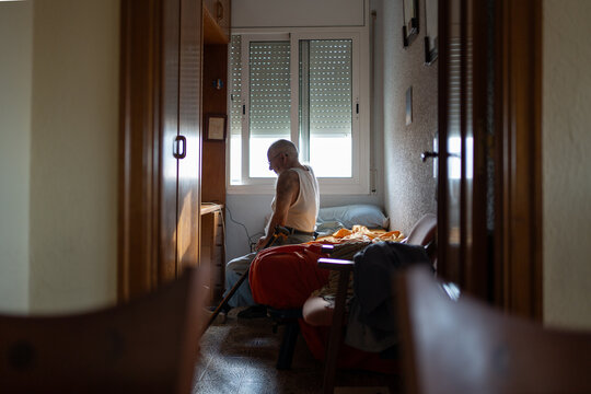 older man sitting on his bed in a single room, cleaning his glasses in the morning. - Powered by Adobe