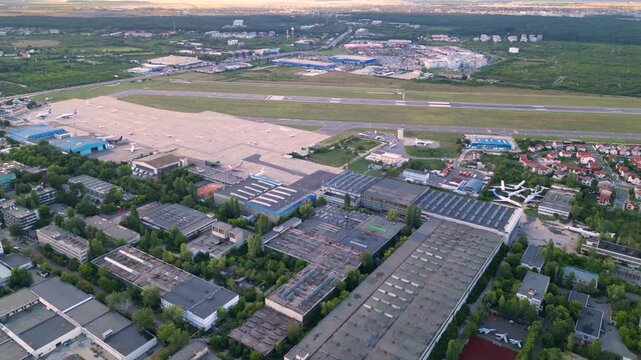 Aerial footage of Bucharest international airport aurel vlaicu on a summer afternoon. Helicopter footage of landing strip, airplanes, hangars and infrastructure surrounding the airfield. 
