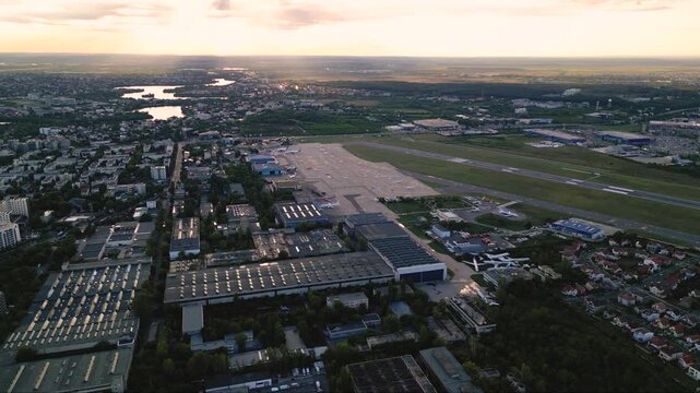 Aerial footage of Bucharest international airport aurel vlaicu on a summer afternoon. Helicopter footage of landing strip, airplanes, hangars and infrastructure surrounding the airfield. 
