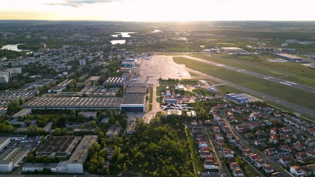 Aerial footage of Bucharest international airport aurel vlaicu on a summer afternoon. Helicopter footage of landing strip, airplanes, hangars and infrastructure surrounding the airfield. 
