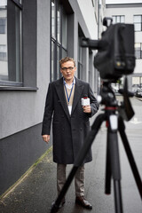 The journalist in glasses stands outside, confidently addressing the microphone