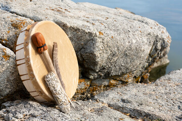 An image of a hand made leather meditation drum leaning on a rock face with sacred feather and sage...