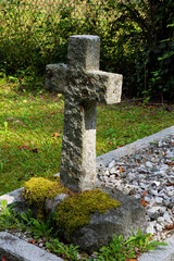 An image of an old weathered stone cross on an unnamed grave.