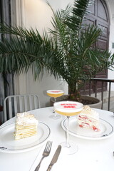 This stylish outdoor café scene features two slices of layered cakes and cocktails with 'KISS ME' printed on the foam. 