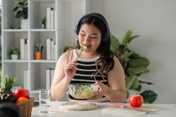 Confident Woman Enjoying a Nutritious Salad at Home While Listening to Music and Embracing a Healthy Lifestyle