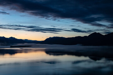 Beautiful fall sunset vibes with a cascading sky transition from peach to deep blues. In the background a low-lying fog hovers over the water, with clouds cascading from the background to foreground.