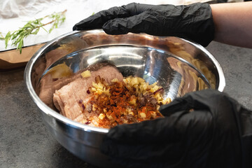 Chief's Hands in black gloves holding metal bowl with mincemeat with ingredients to mix to cook cutlets or meatballs, recipe.