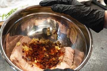 Chief's Hands in black gloves holding metal bowl with mincemeat with ingredients to mix to cook cutlets or meatballs, recipe.