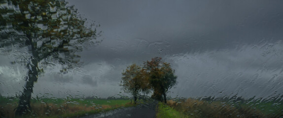 RAIN ON THE ROAD - Water flowing down the glass and dramatic black clouds over fields and country road
