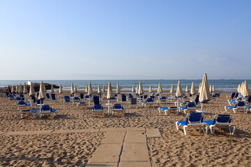 many closed beach umbrellas with sunbeds at a seaside resort near the sea waiting for tourists