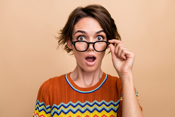 Portrait of impressed speechless person arm touch eyeglasses open mouth isolated on beige color...