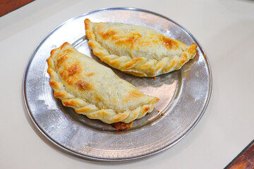 two meat empanadas on a stainless steel plate