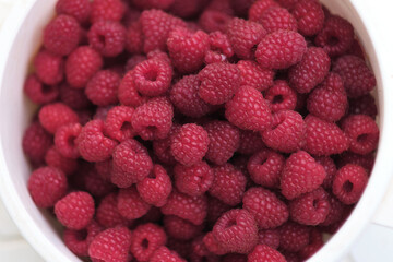 close-up of freshly picked ripe raspberries in a white bowl. vibrant red berries create a visually appealing pattern, showcasing their natural texture and juiciness. freshness and richness of these