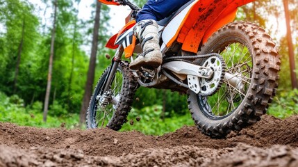 A dirt bike is in the dirt with a person on it. The bike is orange and has a white chain