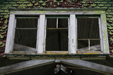 Old broken and cascading asymmetrical window frames surrounded by decaying wood with flaking paint and moss overgrowth.