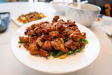 fried sticky ribs marinated in soy sauce and ginger sprinkled on white dish on marble table, chineese style.