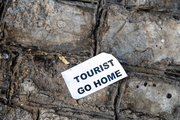 Protest poster with Tourist Go Home against mass tourism on stone wall
