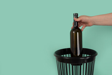 Quitting alcohol concept. Hand throwing wine bottle into trash bin or waste bucket.