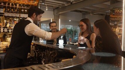 Smart bartender with VIP customer at luxurious bar greeting new beautiful guest at counter in engaging lively conversation at back view in lighting atmosphere at lighting warm nightclub. Vinosity.