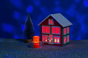 Halloween candle between red and green house with red light in windows and Christmas tree