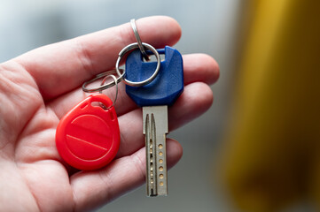 Hand holding a house key with a keychain and RFID fob