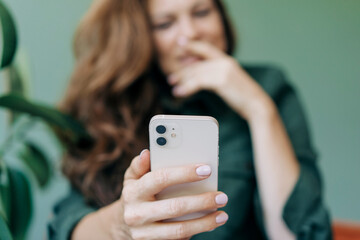 A woman is holding a mobile phone, the woman's face is out of focus, the mobile phone is in the...