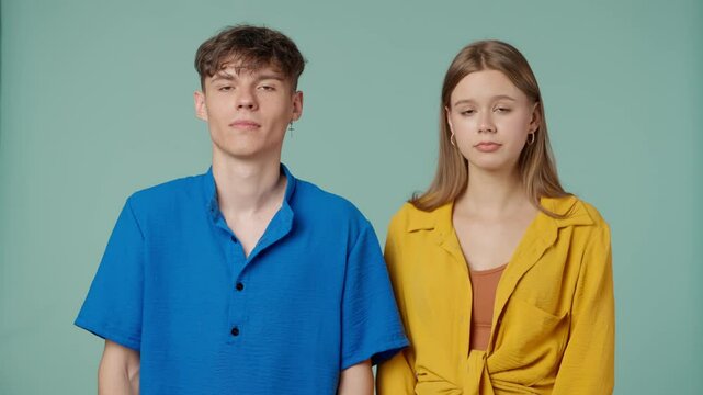 Positive couple of young boyfriend and girlfriend in yellow blue clothes isolated on green background look at camera shrugging with confused face expressions.