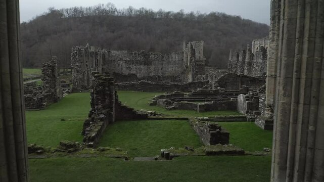 Aerial drone footage of the medieval Rievaulx Abbey ruins in North Yorkshire, showcasing ancient stone structures and green landscapes in England.