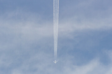 Airplane in the blue sky with white clouds and contrail.