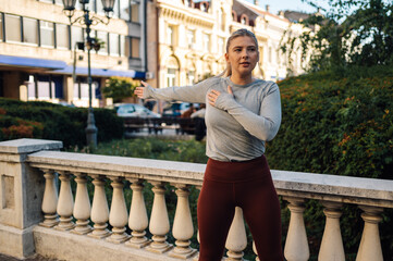 Young sporty woman stretching arms before exercising outdoors