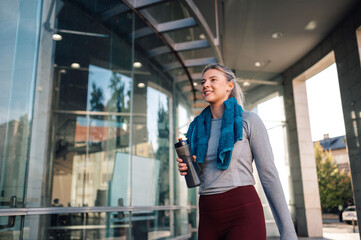 Young sporty woman walking out of the gym holding a bottle of water