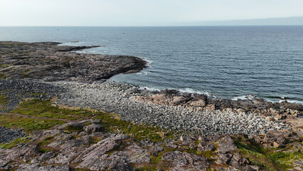 Rocky coastal shore with pebbles and calm ocean waves under a clear sky in a serene natural setting.