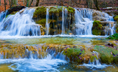 waterfall on small mountain river rushing through canyon covered by red dry leaves