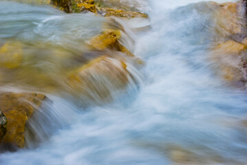 waterfall on small mountain river rushing through canyon covered by red dry leaves