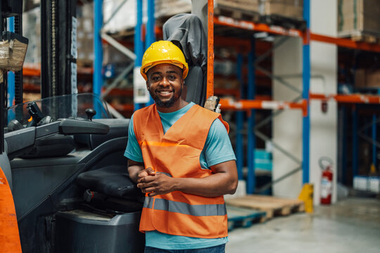 Smiling warehouse worker posing by forklift in busy warehouse