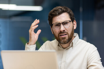 Close-up portrait of an angry and frustrated young male office worker sitting at a workplace with a...
