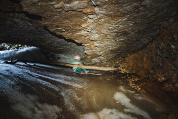 In a dimly lit cave, a person stands firmly grasping a sturdy wooden stick, indicating they might...