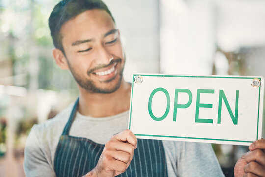 Small business, asian man and smile with open sign by window, information and announcement to client. Male person, barista and happy with poster for cafe, coffee shop and excited for customer service